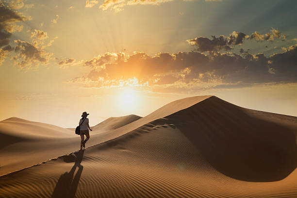 A young woman climbing a giant sand dune in a desert at sunset in the Empty Quarter, or Rub al Khali,  the world's largest sand desert